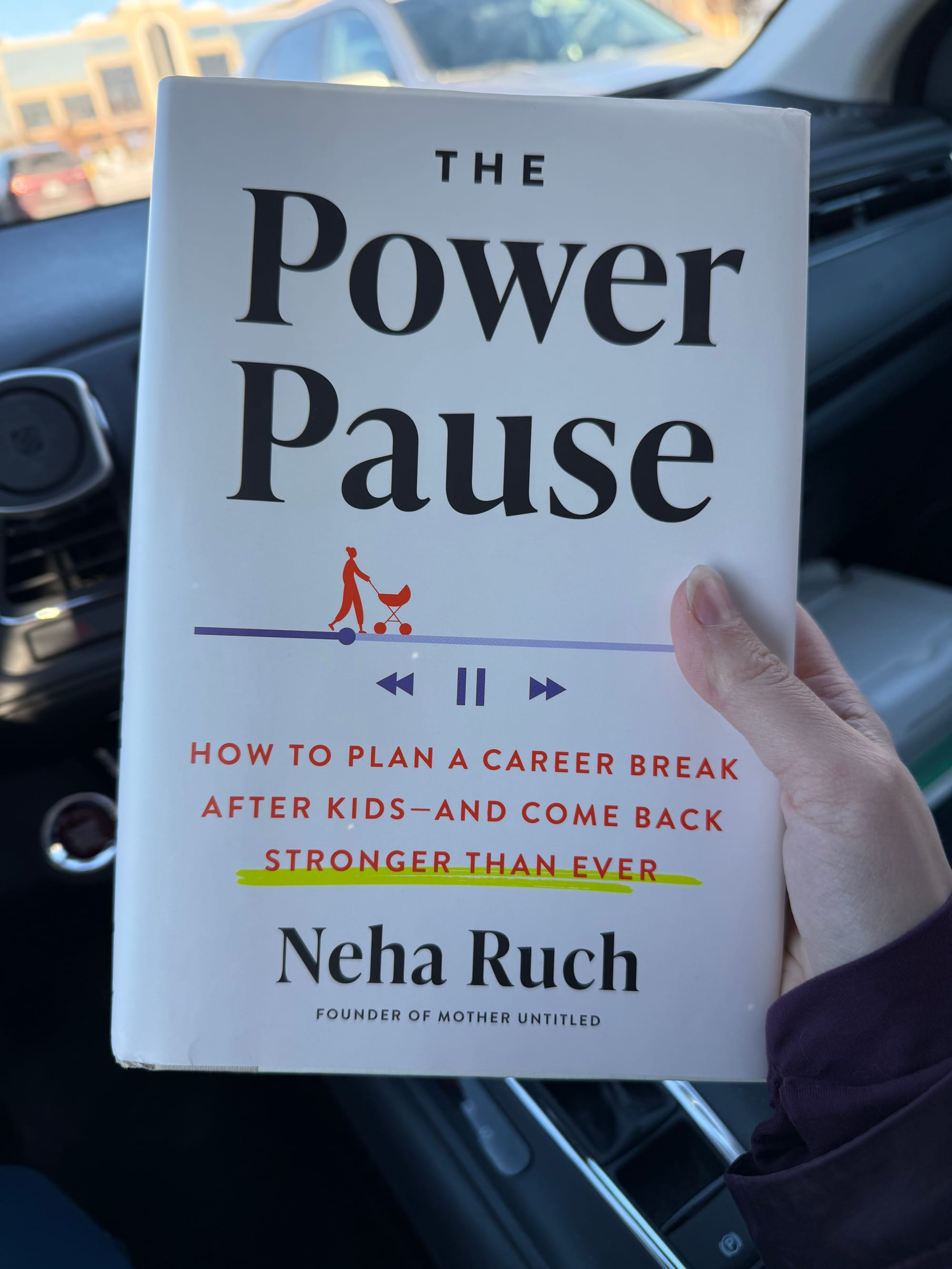 A hand holding a hardcover copy of The Power Pause by Neha Ruch in a car.