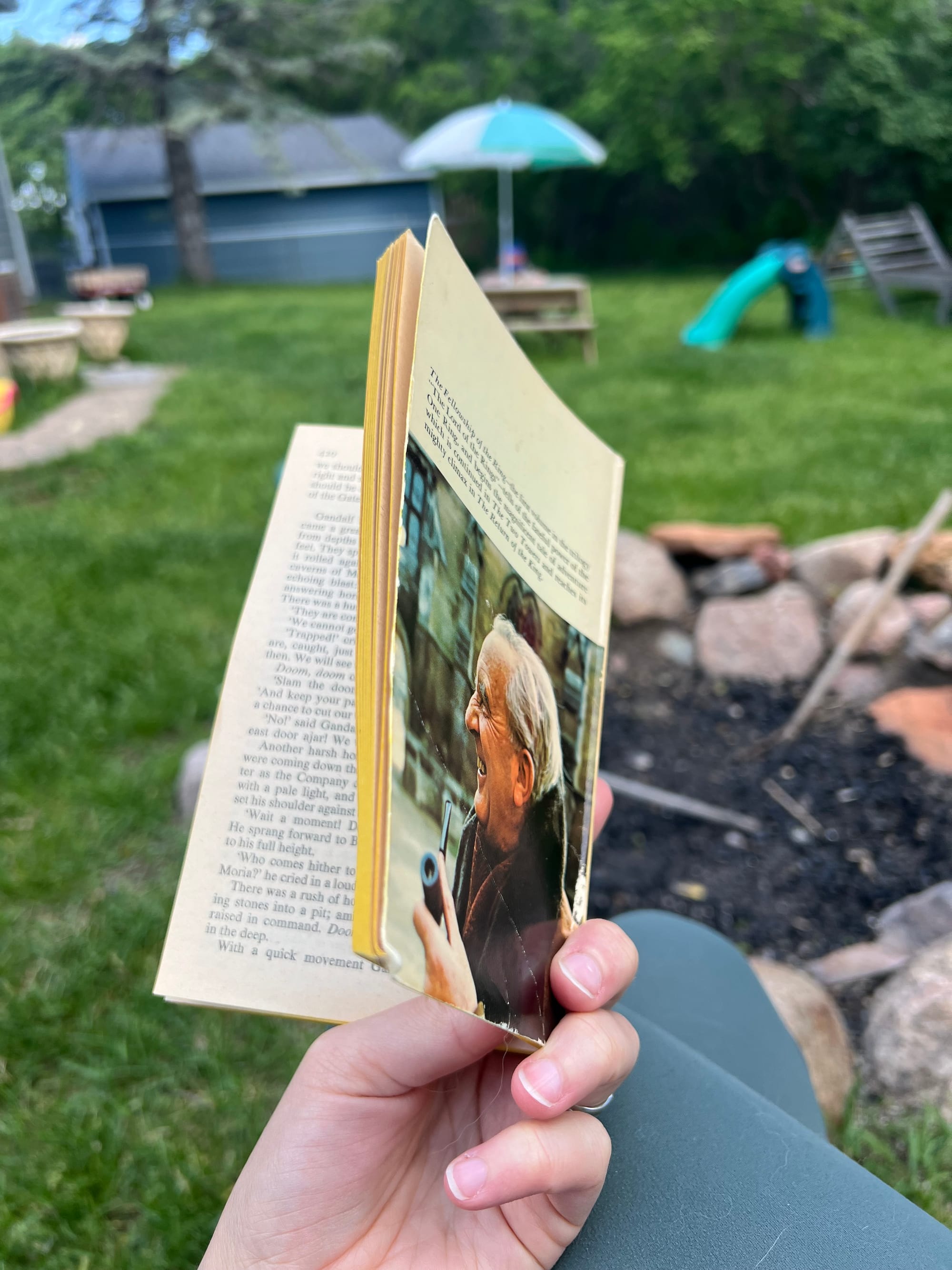 A woman holding a paperback copy of The Fellowship Of The Ring by J.R.R. Tolkien sitting outside in a backyard.