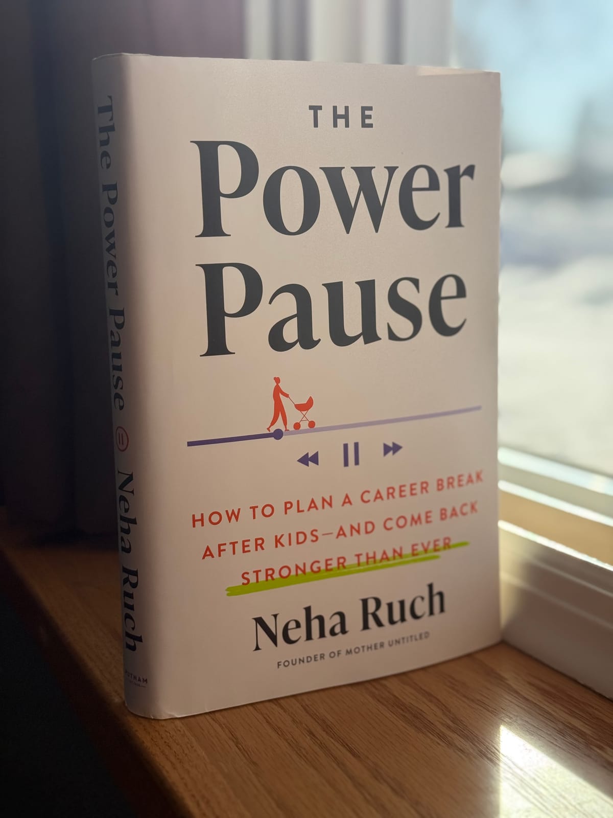 A hardcover copy of The Power Pause by Neha Ruch standing on a windowsill in front of a sunny window.