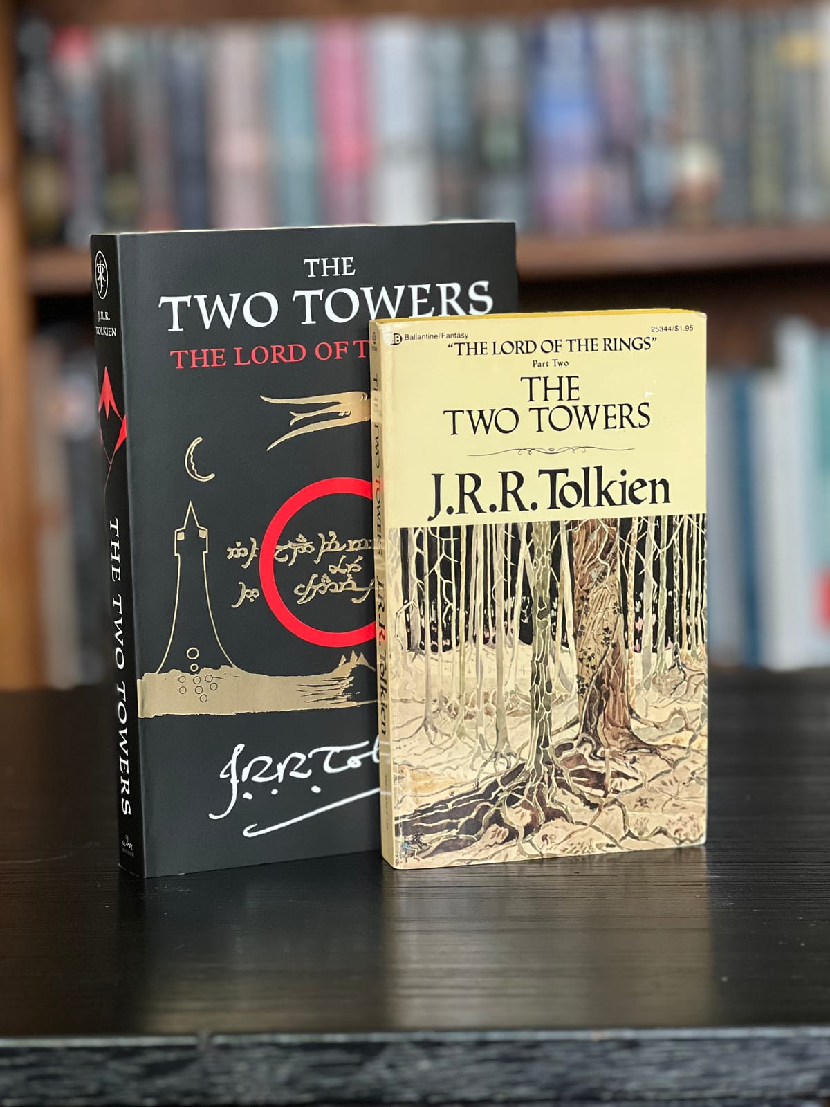 Two paperback copies of The Two Towers by J.R.R. Tolkien standing on a table in front of a stuffed bookcase.