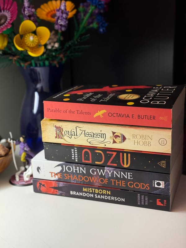 A stack of books on a white desk, including Parable of The Talents, Dune, and Mistborn.