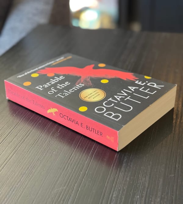 A paperback copy of Parable of The Talents by Octavia E. Butler lying on a black side table.