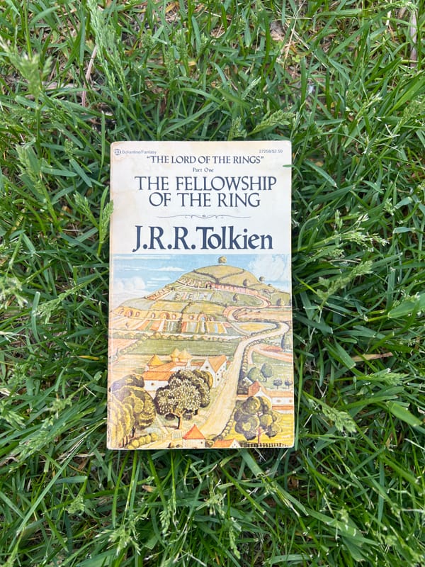 A paperback copy of The Fellowship Of The Ring by J.R.R. Tolkien lying on green grass.