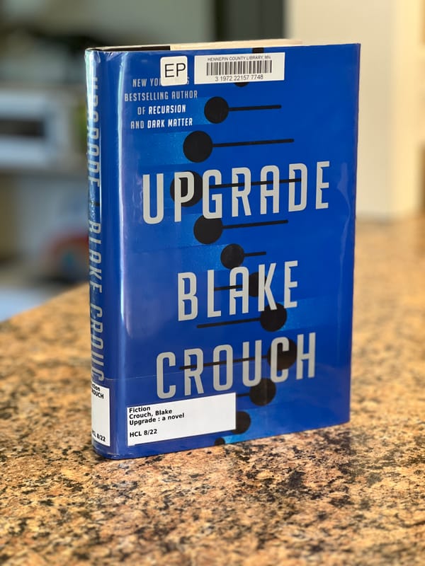 A hardcover library copy of Upgrade by Blake Crouch stands on a granite countertop.