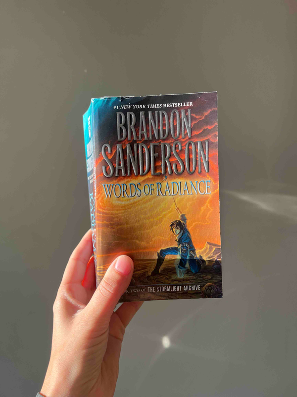 A hand holding up a paperback copy of Words of Radiance by Brandon Sanderson.