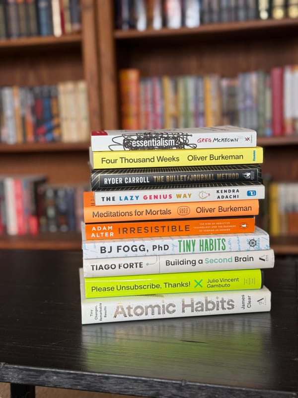 A stack of self-help non-fiction books on a black side table in front of a stuffed bookcase.