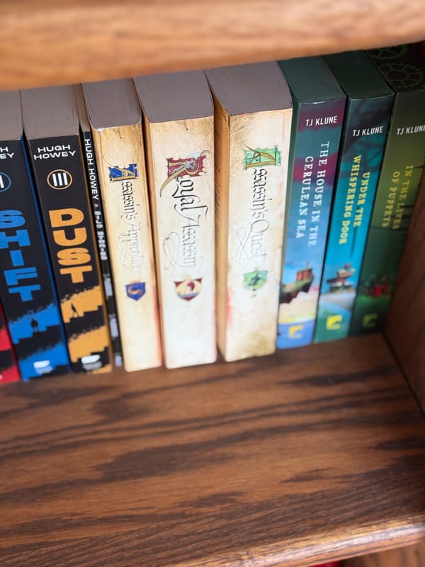 View of a stuffed bookshelf including the Farseer Trilogy by Robin Hobb.